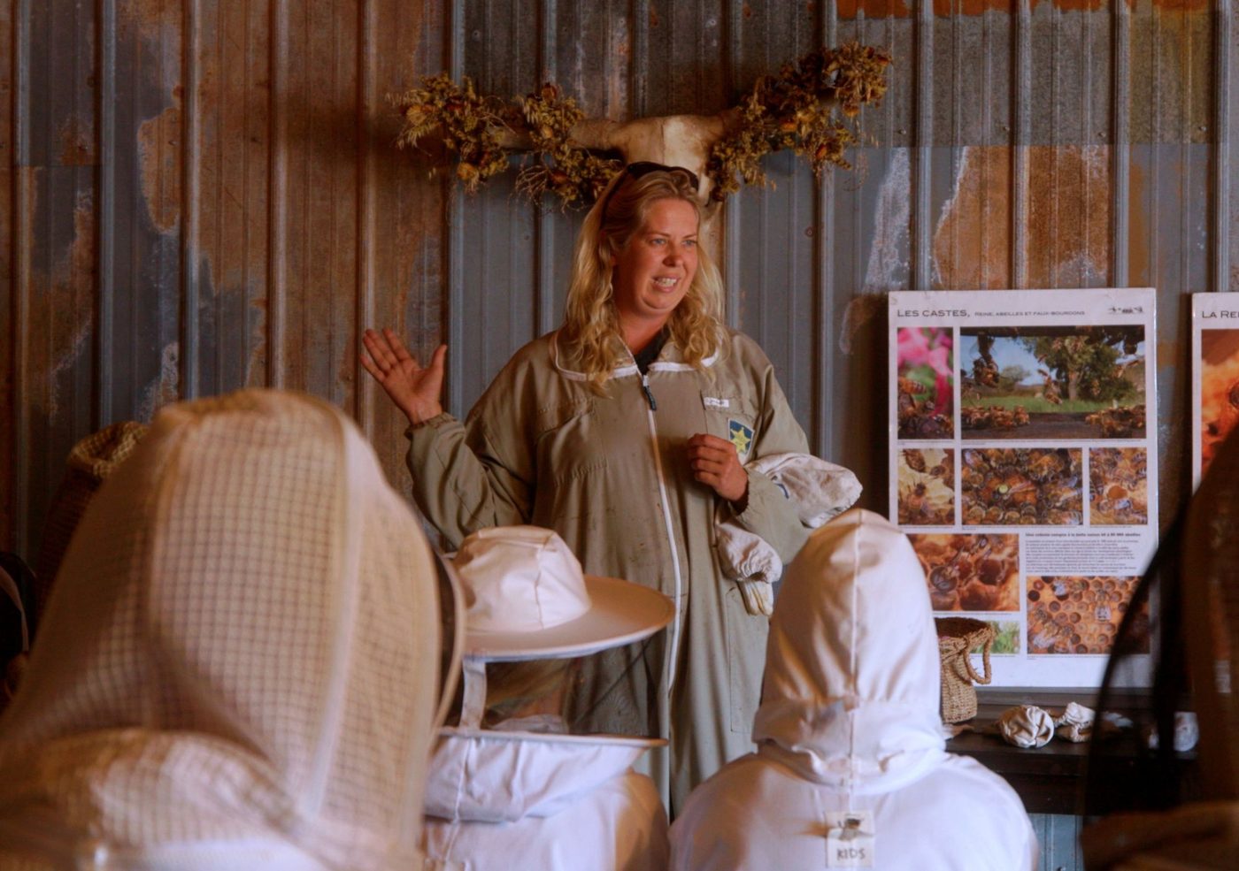 The business owner, in a beekeeping suit, teaching a class of students in veiled hats