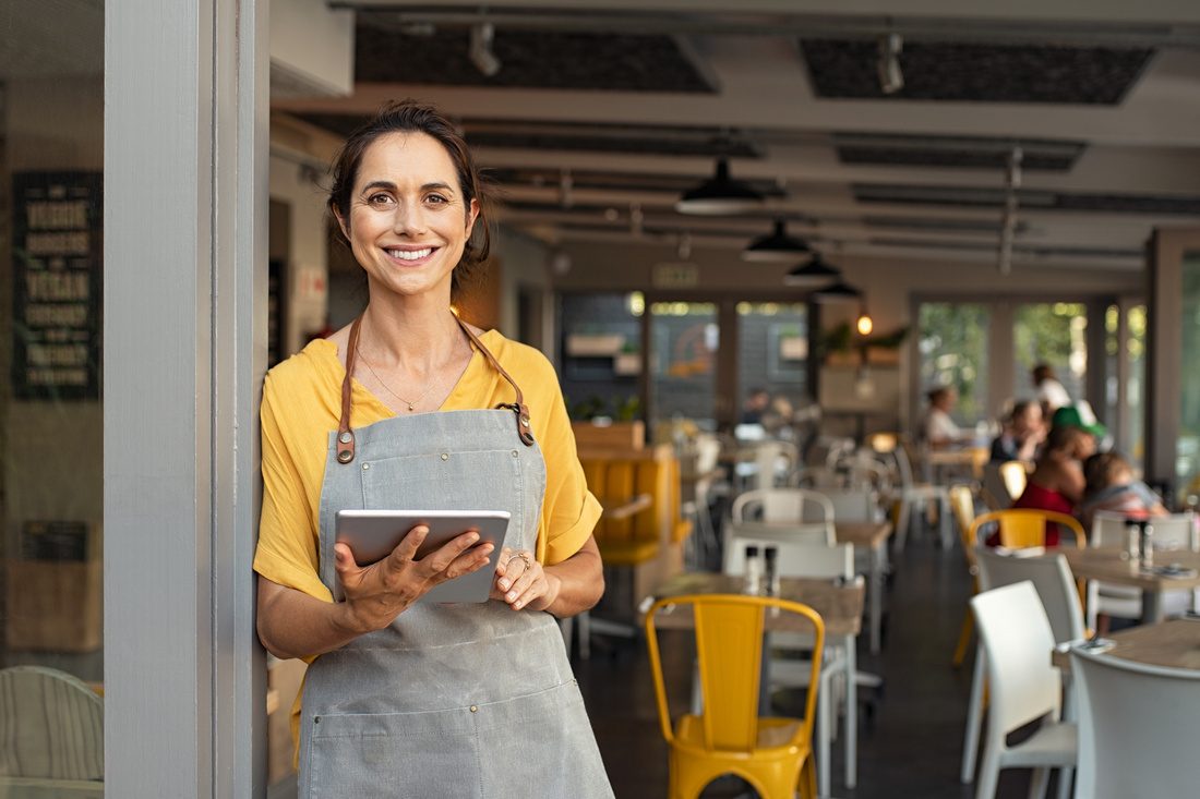A café owner standing in her doorway holding a tablet